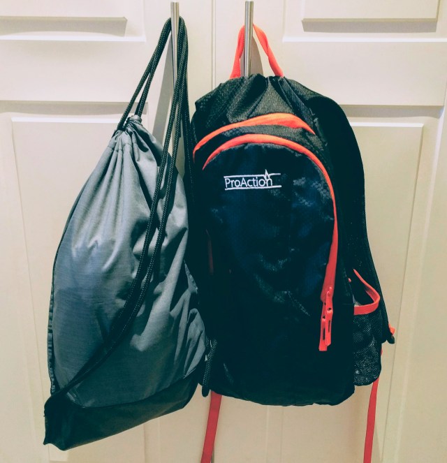 A school rucksack and a PE Kit bag hanging on the door handle all packed and ready for school.