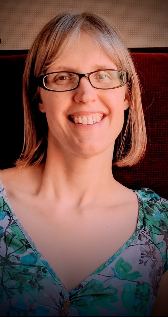 Author of Creating Calm With Clare is introducing herself by way of a photograph in which she is smiling. Clare is wearing her glasses and is dressed in a patterned green top.